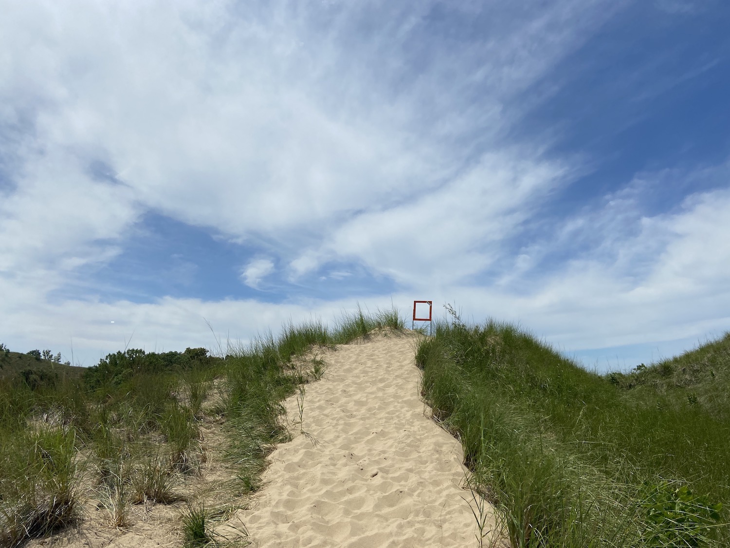 A sand dune in Michigan with an empty frame meant to hold a trail info sign on top of the dune.